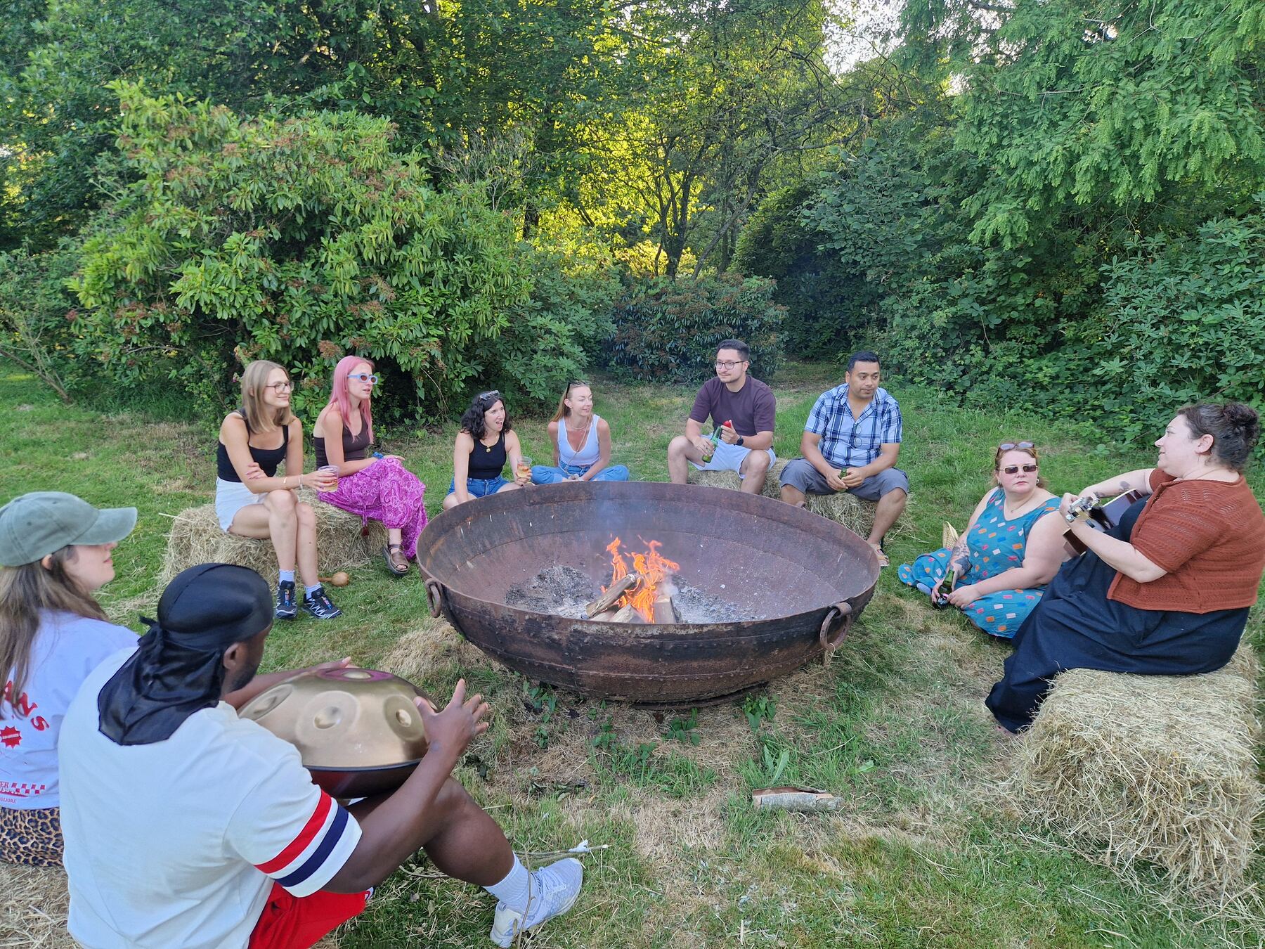 People sitting close around the fire in the evening, one playing a drum