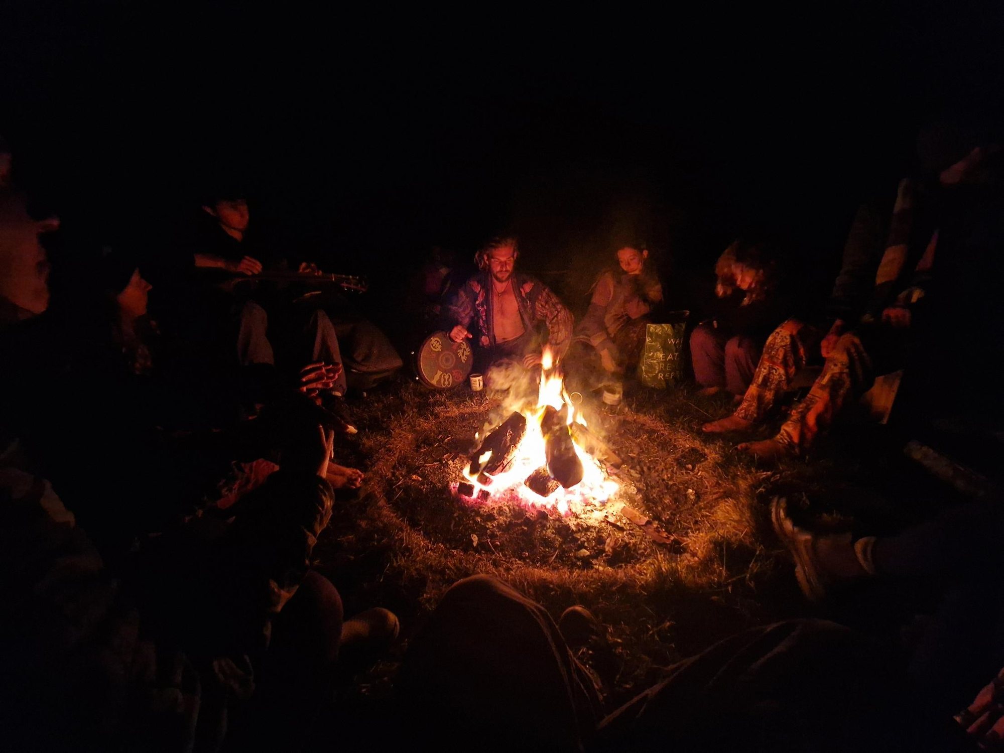 Artists around the fire at night, a drum and a guitar, faces lit by the flame