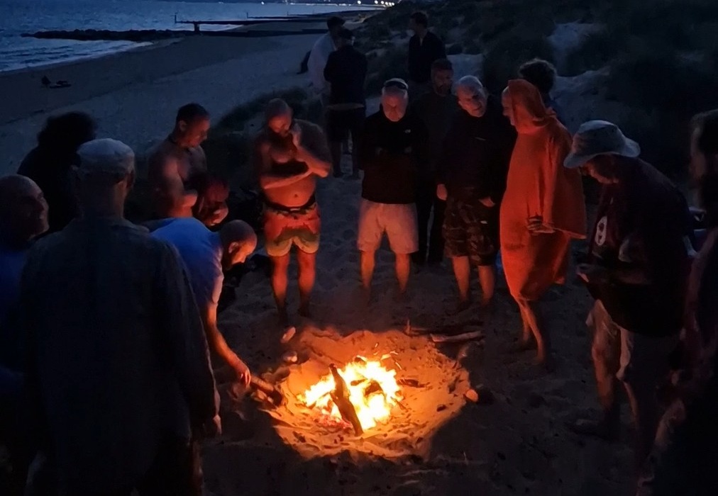 Men standing around a fire on the beach at dusk