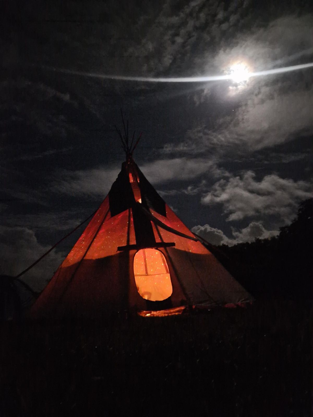 The tipi lit from within under a full moon