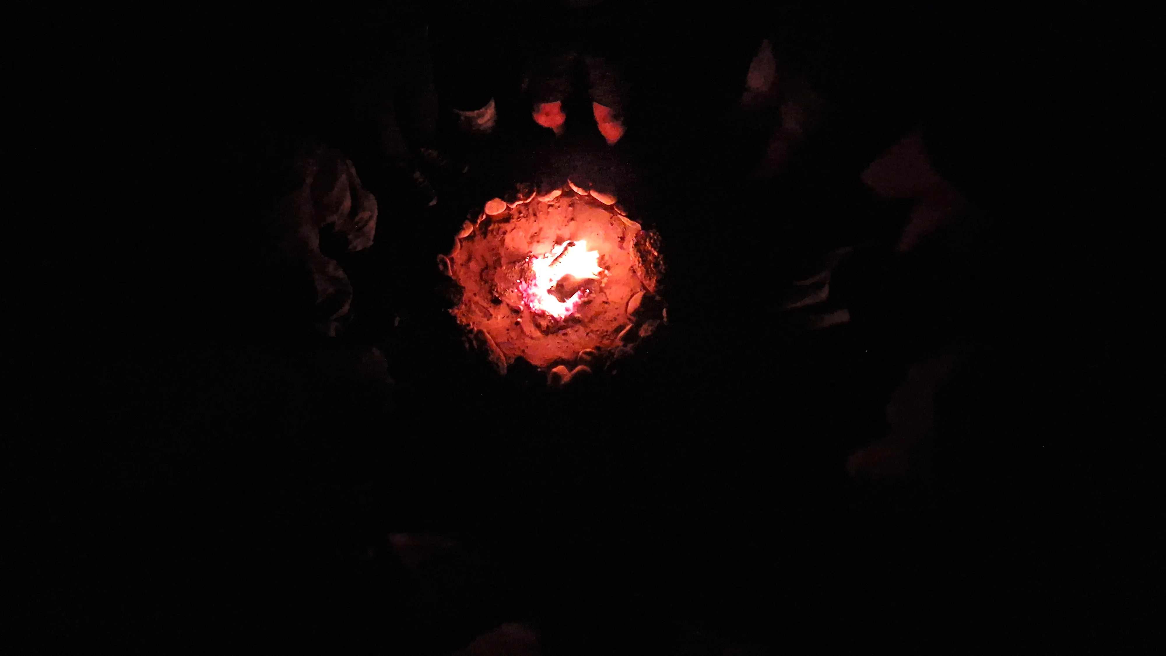 Hands held out over a small fire ring in the dark