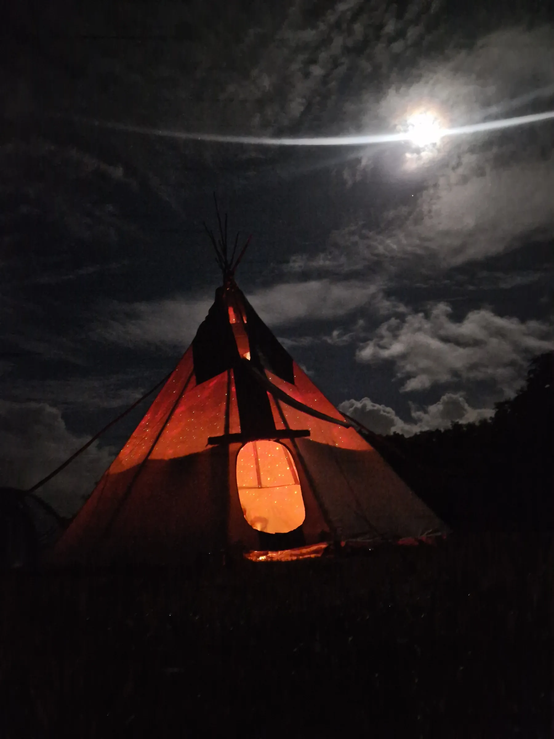 The tipi glowing red under a full moon
